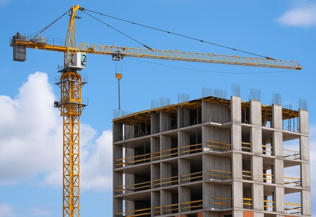 Yellow tower crane beside a multi-story concrete building under construction.